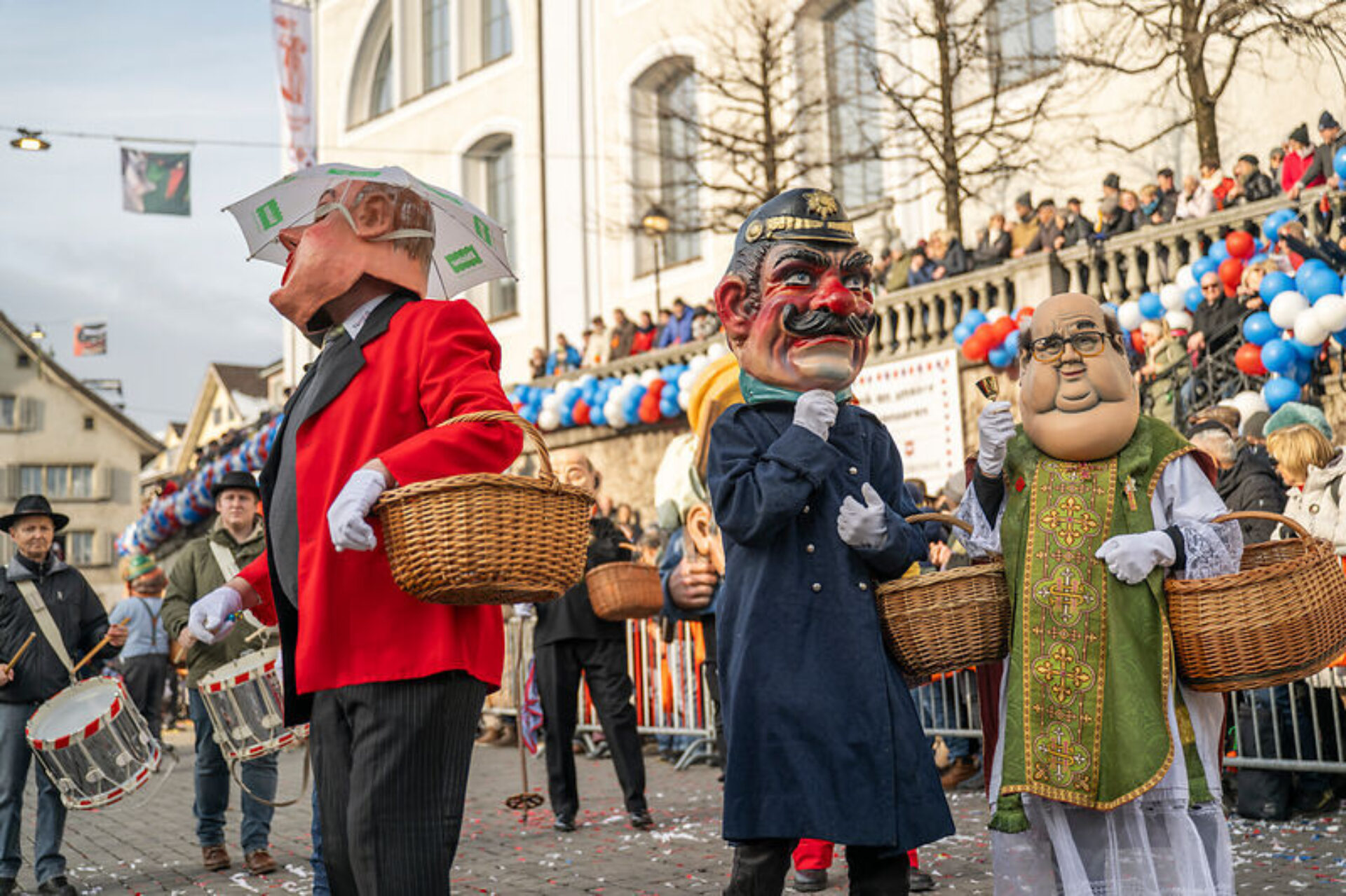 Drei Grossgrinde, traditionelle Fasnachtsfiguren mit grossen Kopfmasken, laufen durch die fastnächtlichen Gassen von Schwyz.