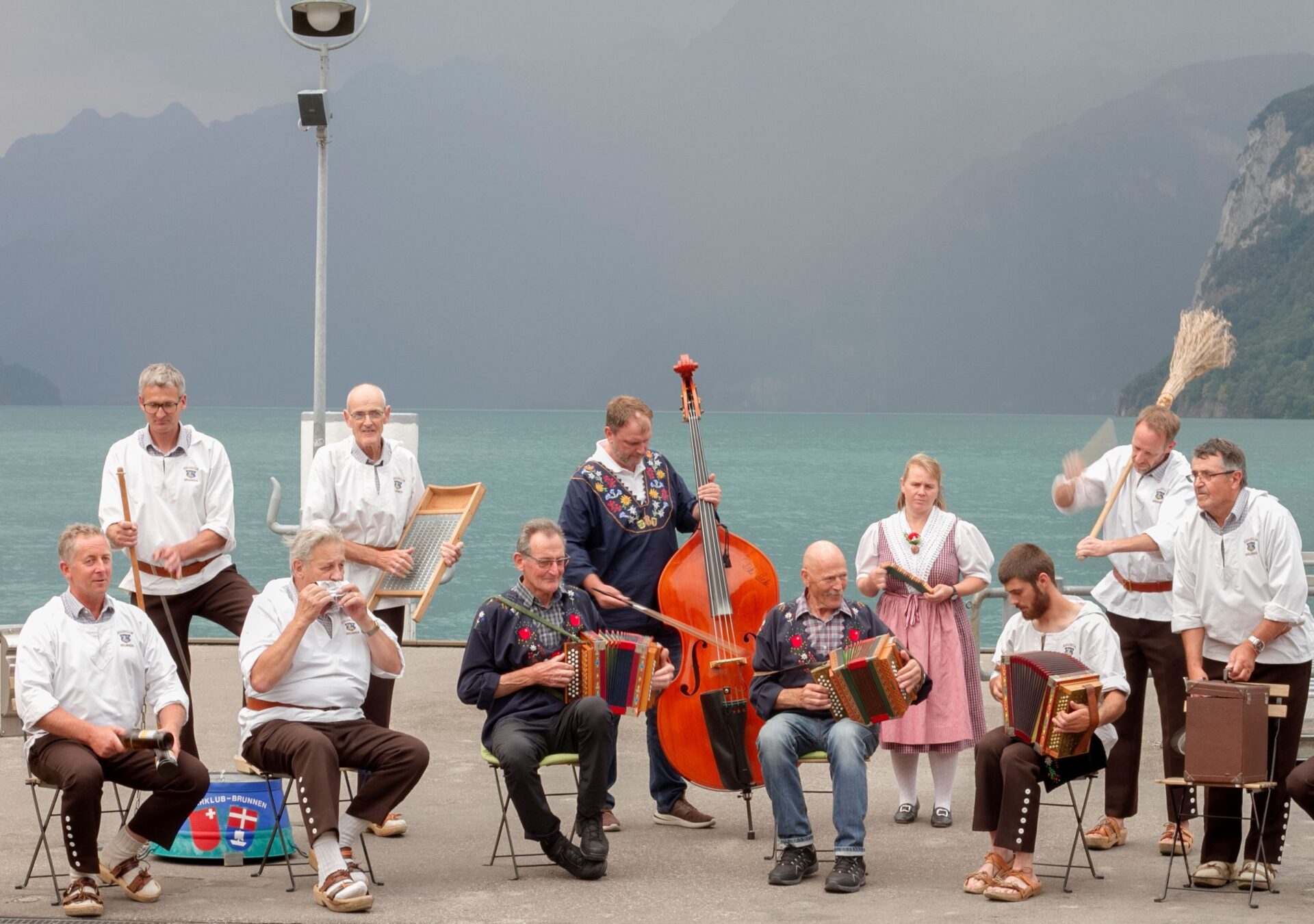 Folkloreshow der Erlebnisregion Mythen mit dem Jodlerclub Brunnen. Die Mitglieder des Jodlerclubs in traditioneller Kleidung spielen Schweizer Volksmusik vor dem Urnersee.