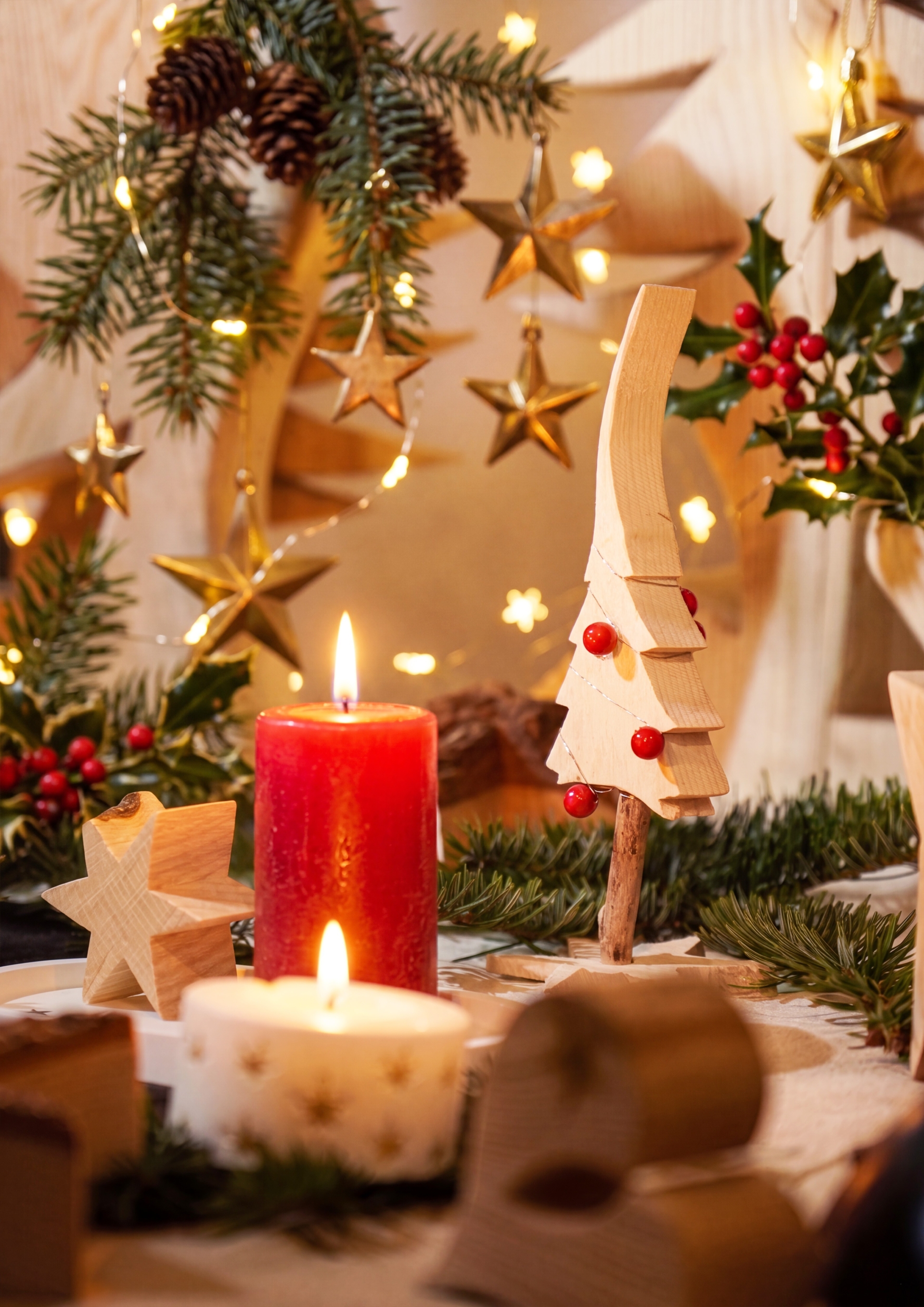 Weihnachtliche Dekoration mit Holzfiguren, Tannenzweigen, goldenen Sternen, Lichterkette und brennenden Kerzen.