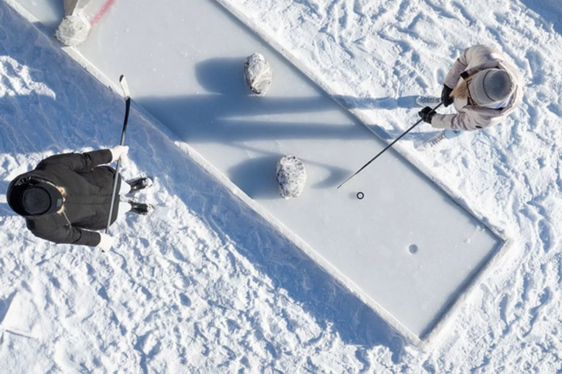 Bick von oben auf eine Eis-Minigolfbahn auf Sattel-Hochstuckli. Zwei Personen in Winterkleidung stehen im Schnee um die Bahn und besprechen den nächsten Schlag.