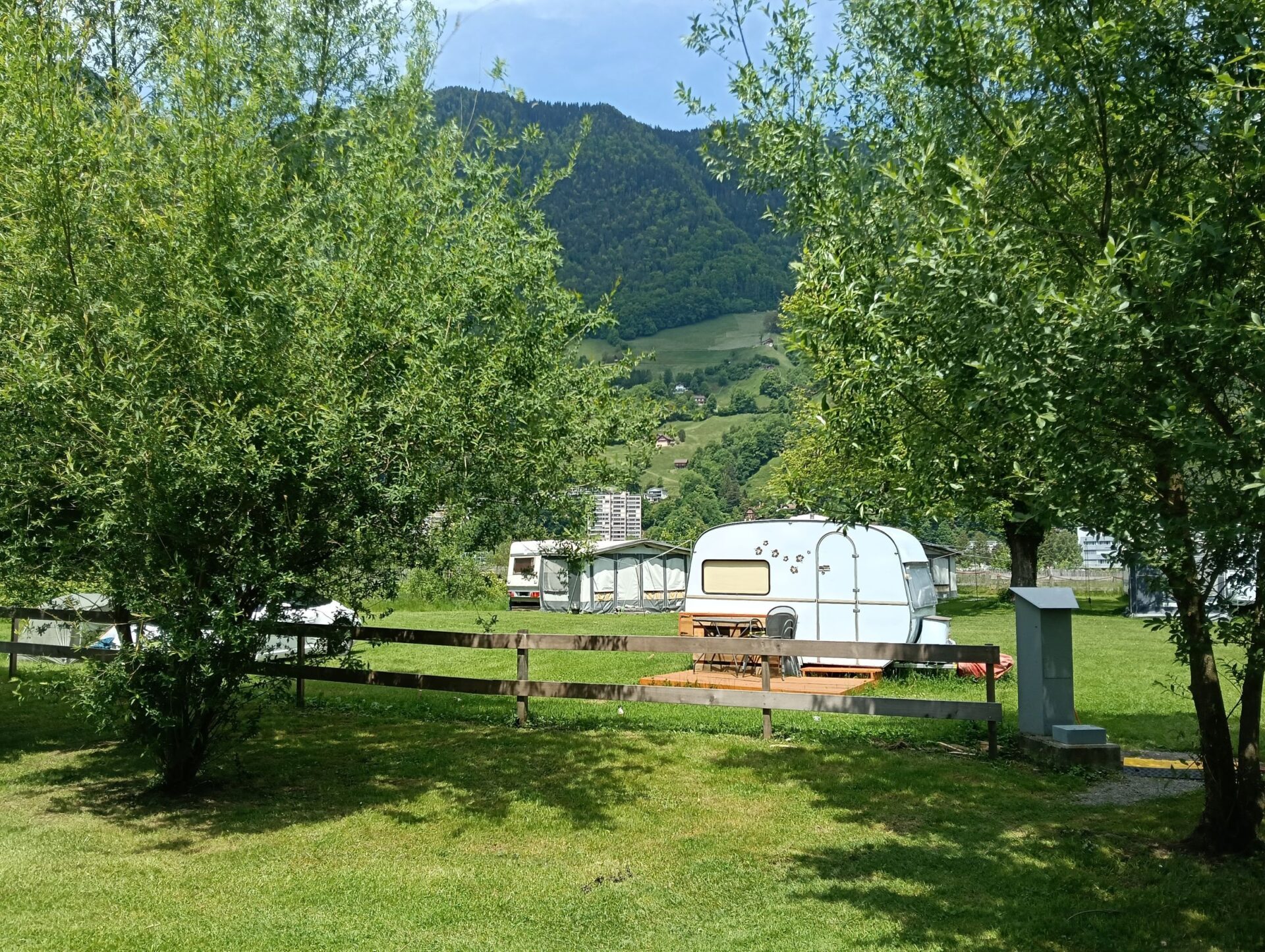 Ein nostalgischer Wohnwagen steht auf dem Campingplatz Hopfräben. Idyllisch umgeben von kleineren Bäumen. Der Untergrund ist Wiese.