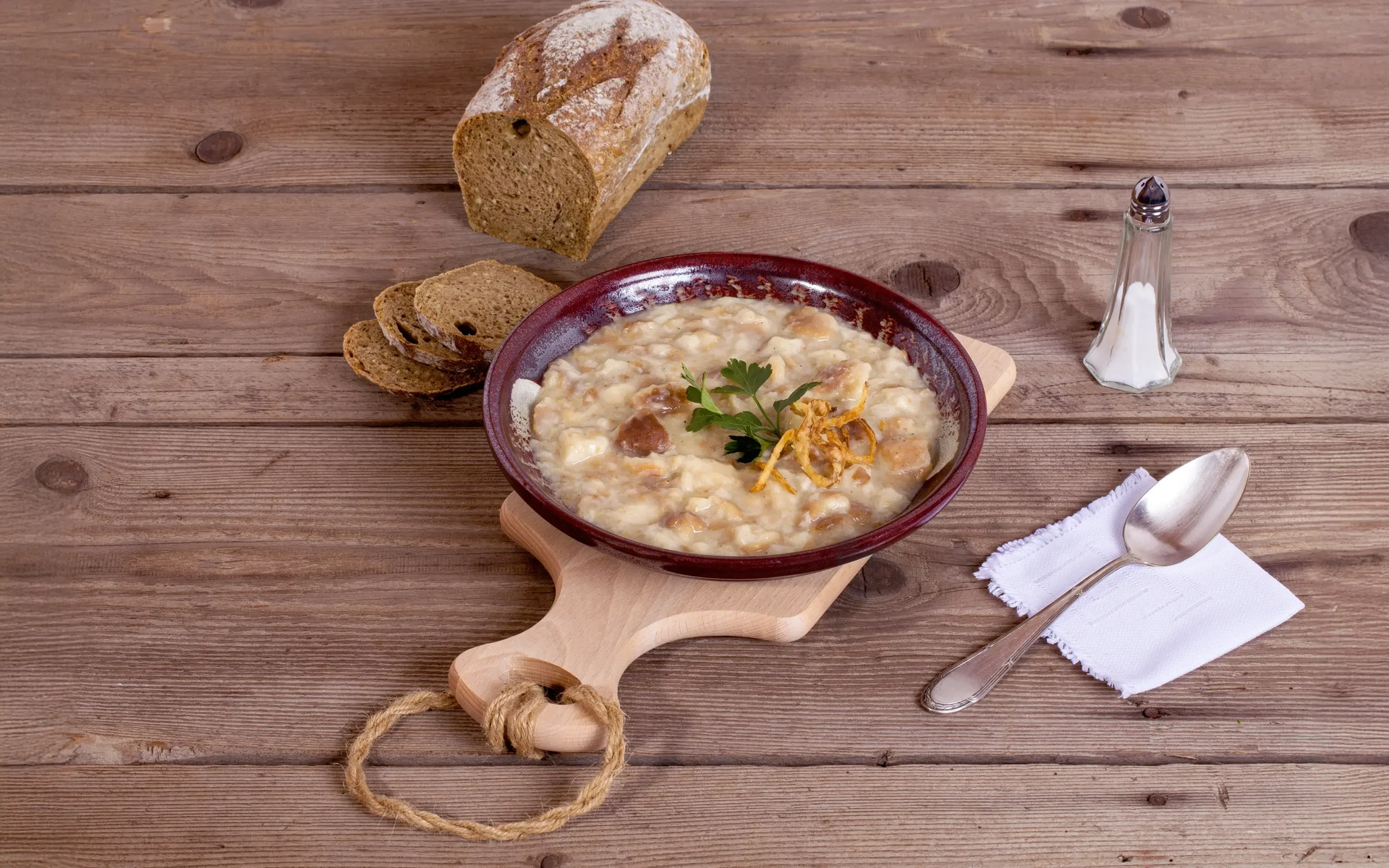 Ein Teller mit angerichteter Käsesuppe, Salzstreuer, Löffel und Brot.