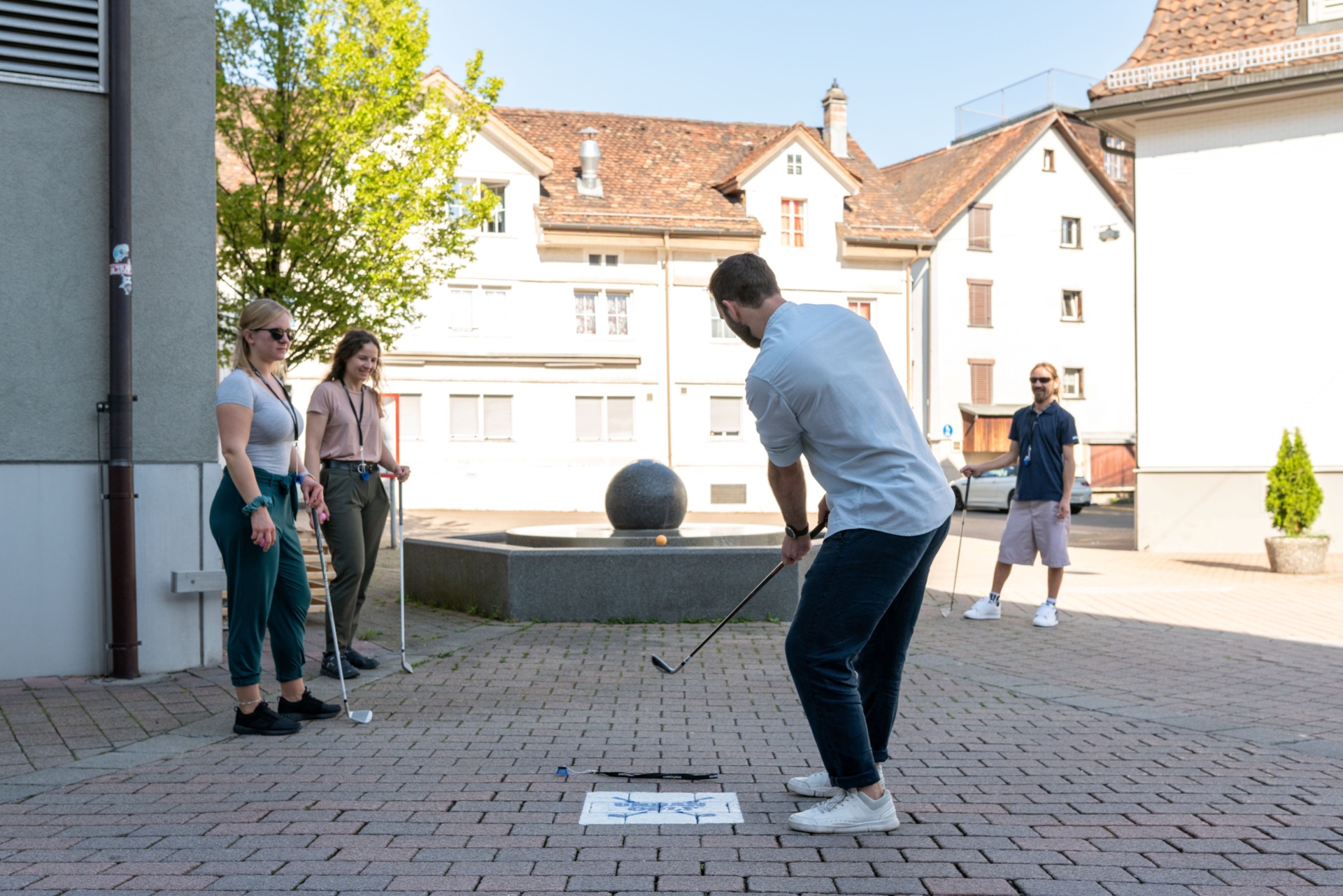 Eine Gruppe von vier jungen Leuten spielt Urban Golf mitten im Dorf Einsiedeln.