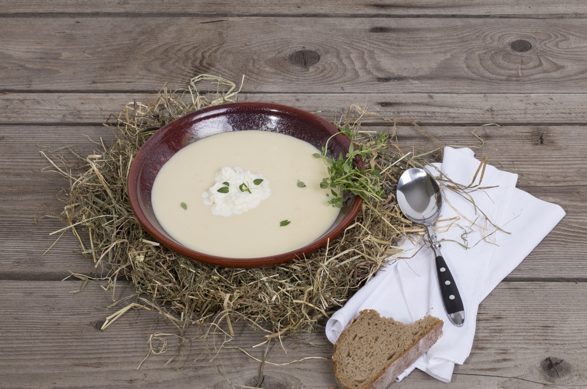 Heusuppe in Schale angerichtet auf Heubett, weisse Serviette Löffel und ein Stück Brot.