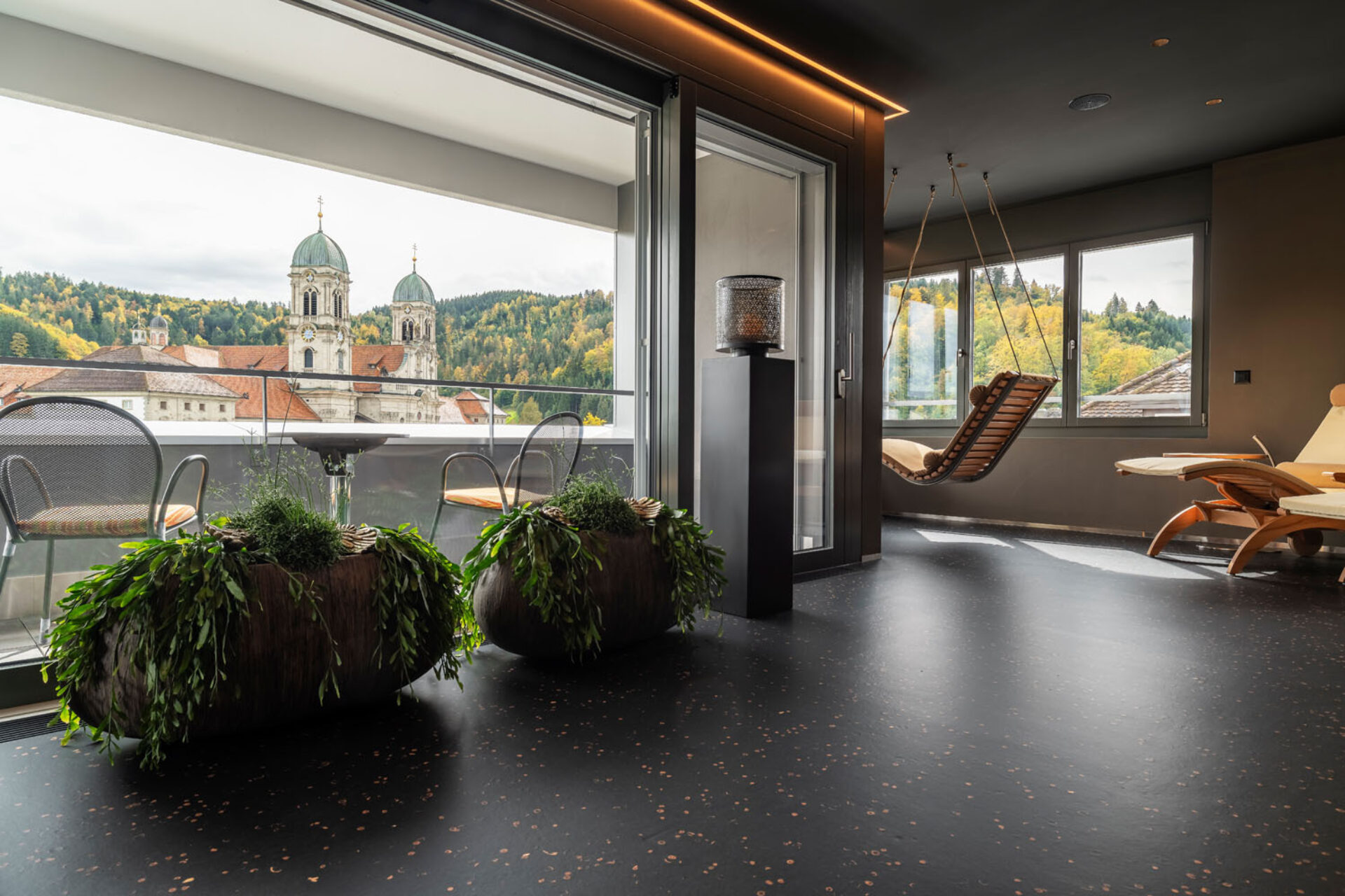 Ruheraum vom Wellenbereich im Hotel Drei Könige mit Liegestühlen, Hängesessel und Blick auf die Türme vom Kloster Einsiedeln.