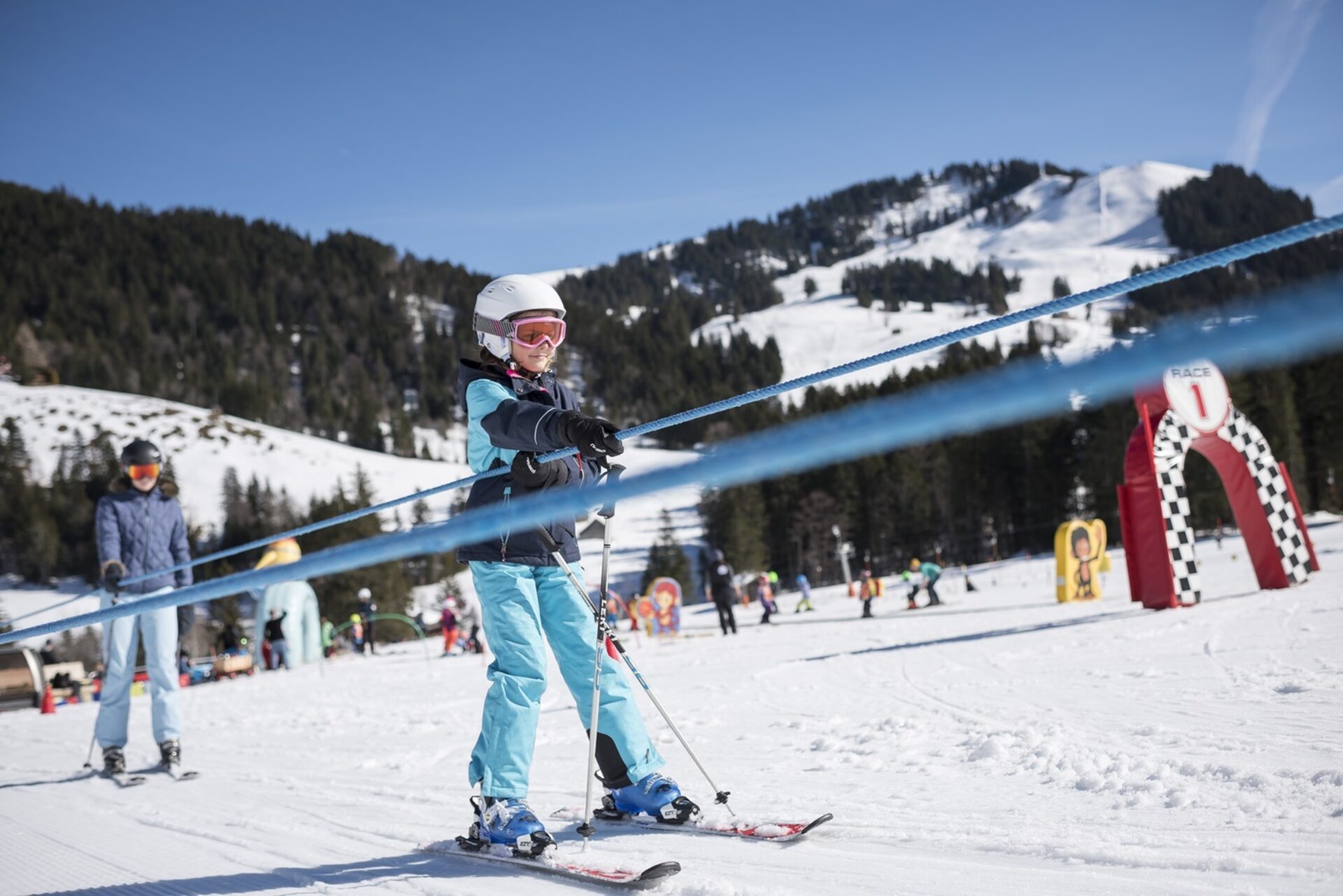 Kinder lassen sich von blauem Seil die Piste hochziehen im Kinderland auf Sattel Hochstuckli.