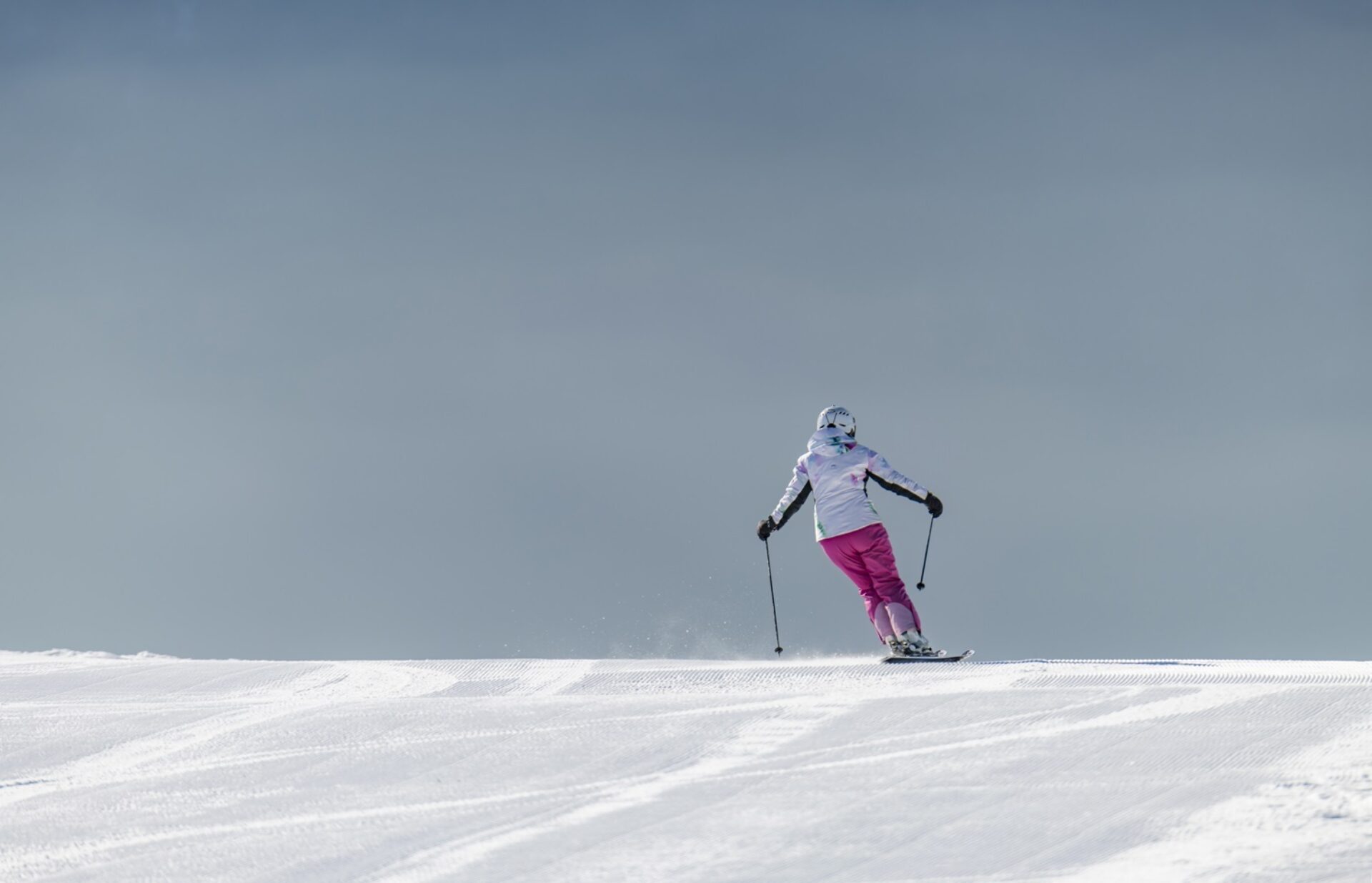 Skifahrerin von hinten in pinken Skihosen auf frisch präparierte Skipiste unterwegs.