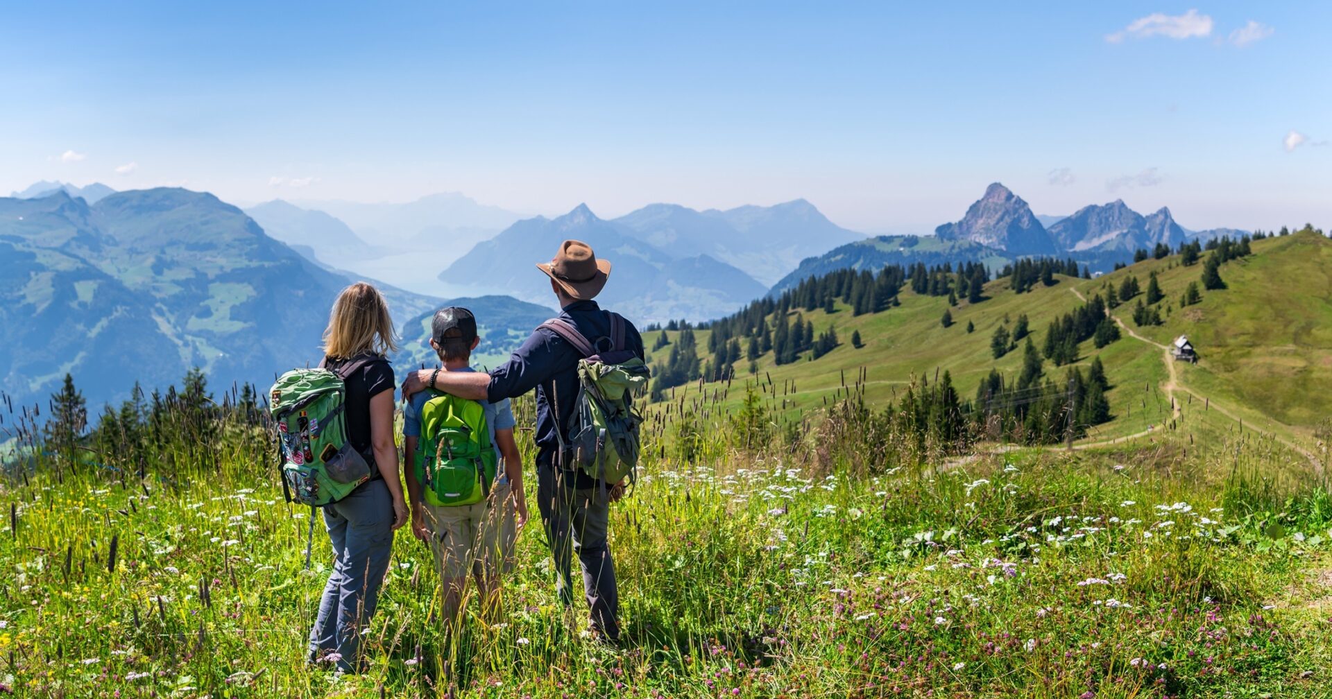 Frau und Mann in der mitte ein Kind beim Wandern. Blick ins Tal. Herrliche Bergwiese Bergpanorama.