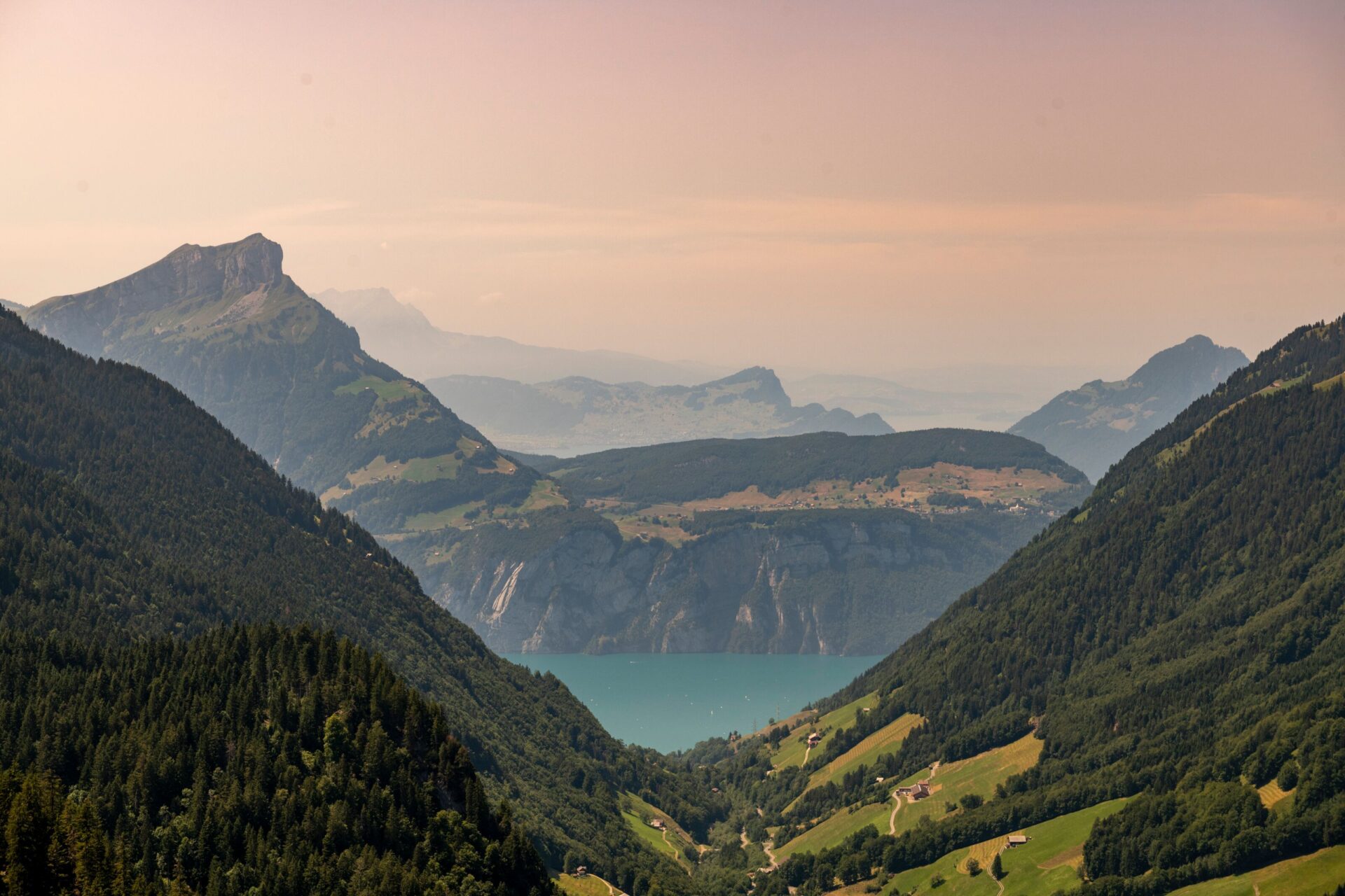 Ein malerisches Tal öffnet sich zu einem türkisfarbenen See, umgeben von sanften Berghängen und unter einem pastellfarbenen Abendhimmel. Die Szene strahlt Ruhe und eine stimmungsvolle Weite aus.