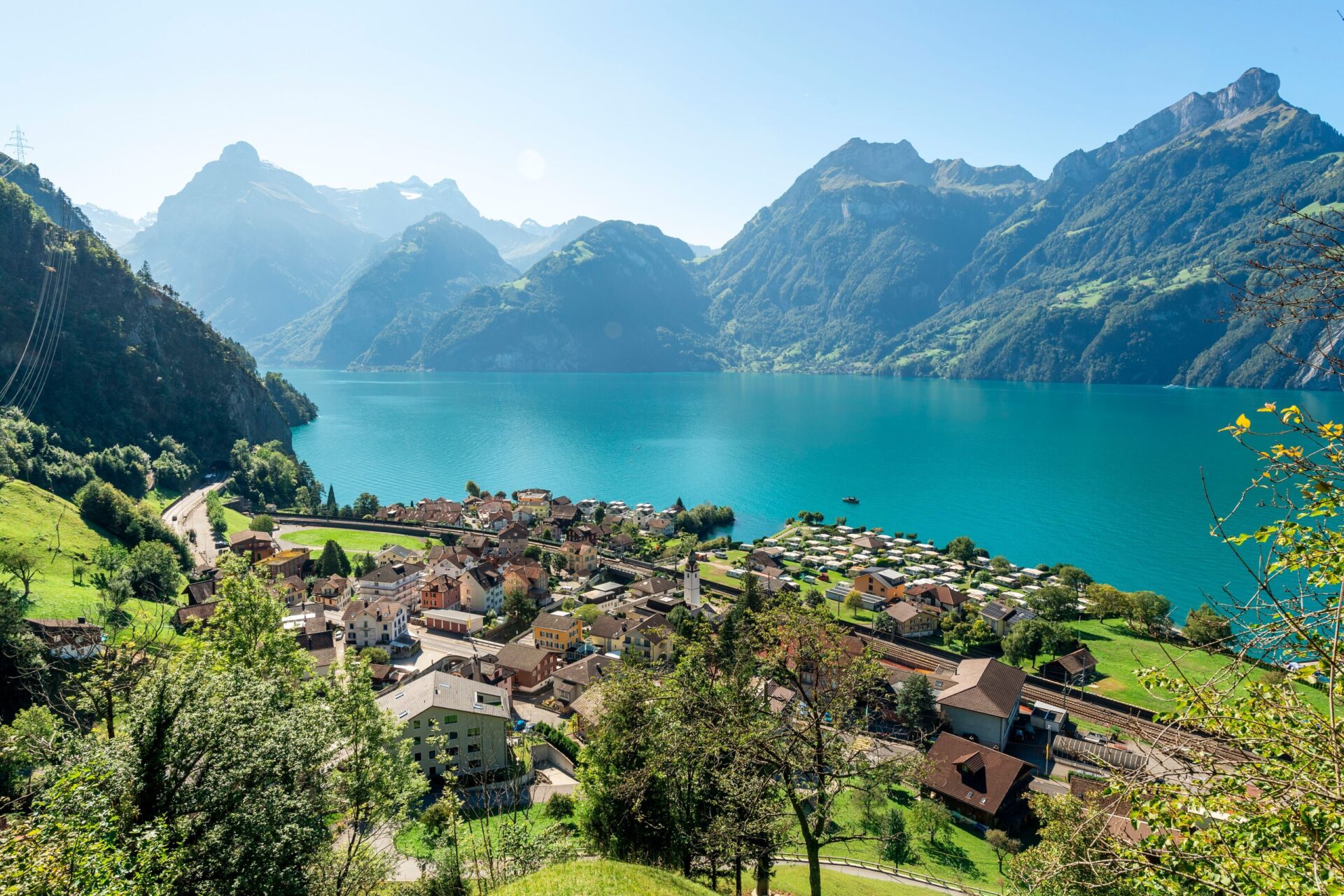 Das Dorf Sisikon liegt idyllisch am Ufer des türkisblauen Vierwaldstättersees, umgeben von majestätischen Bergen und üppigem Grün. Die klare Sicht und das friedliche Ambiente betonen die Schönheit und Ruhe der Schweizer Landschaft.